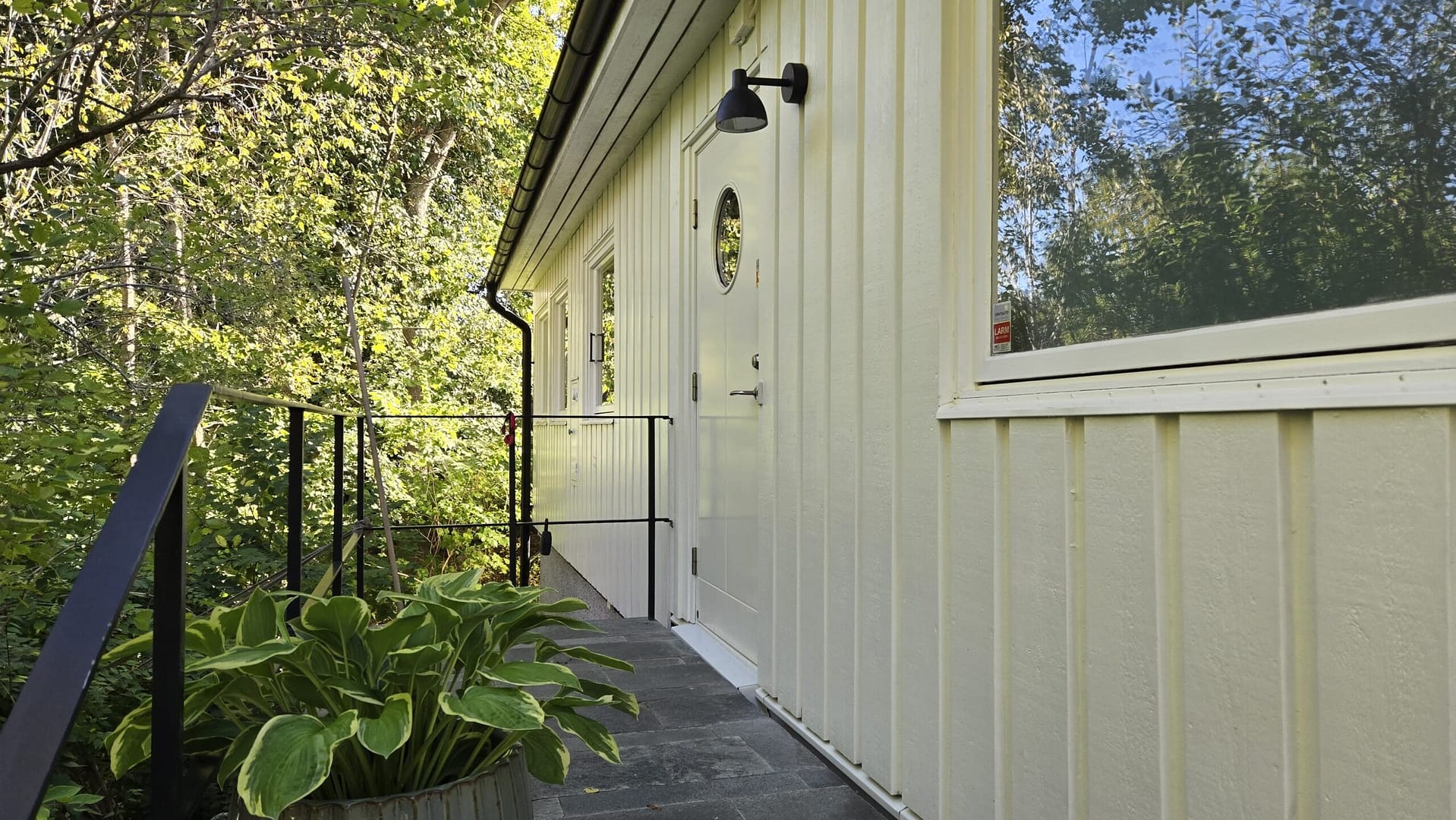 Nyrenoverad husfasad med trappa och svart räcke, omgivet av grönska i Lidingö